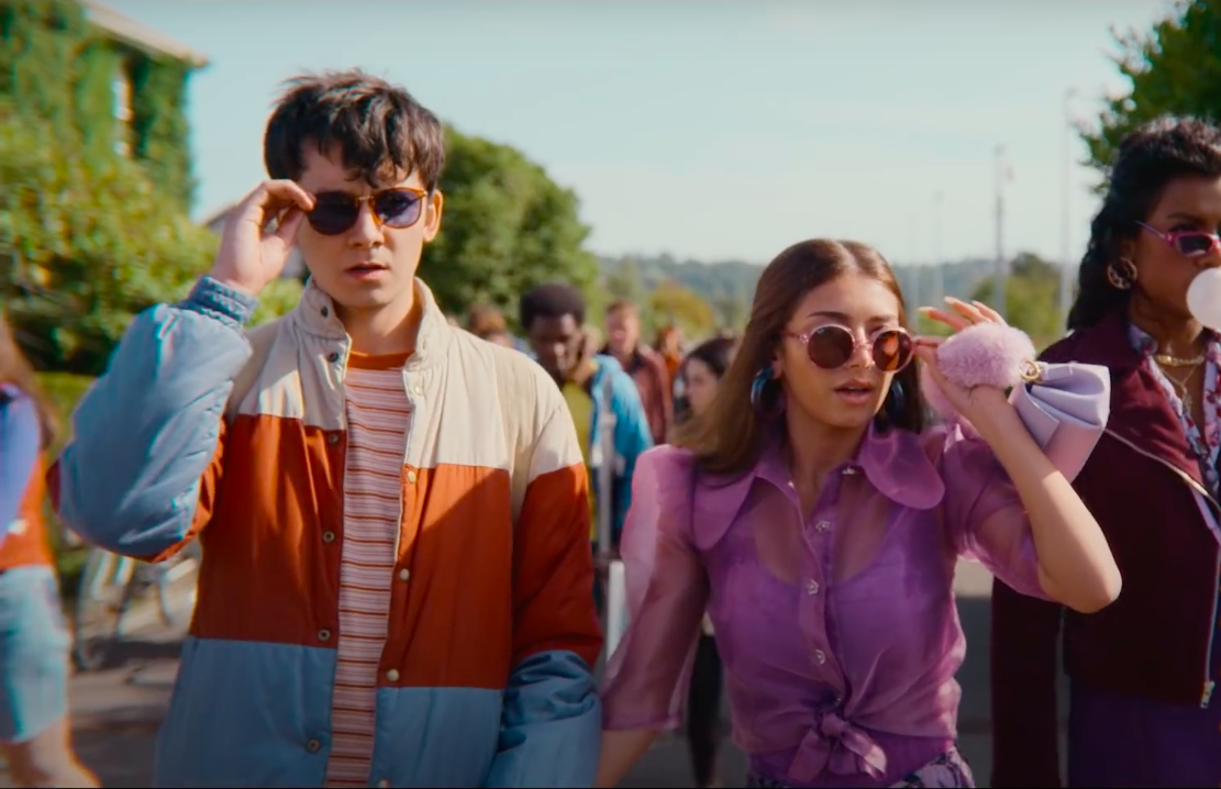 A still from Season 3 of Sex Education featuring Otis and Ruby walking hand in hand about to push down their sunglasses